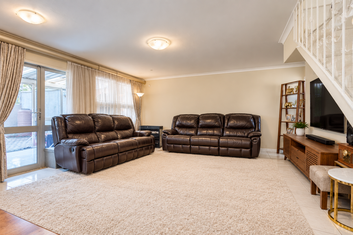 Spacious living room featuring tiled flooring, neutral walls, and a staircase with a decorative metal balustrade, leading out to a patio area.