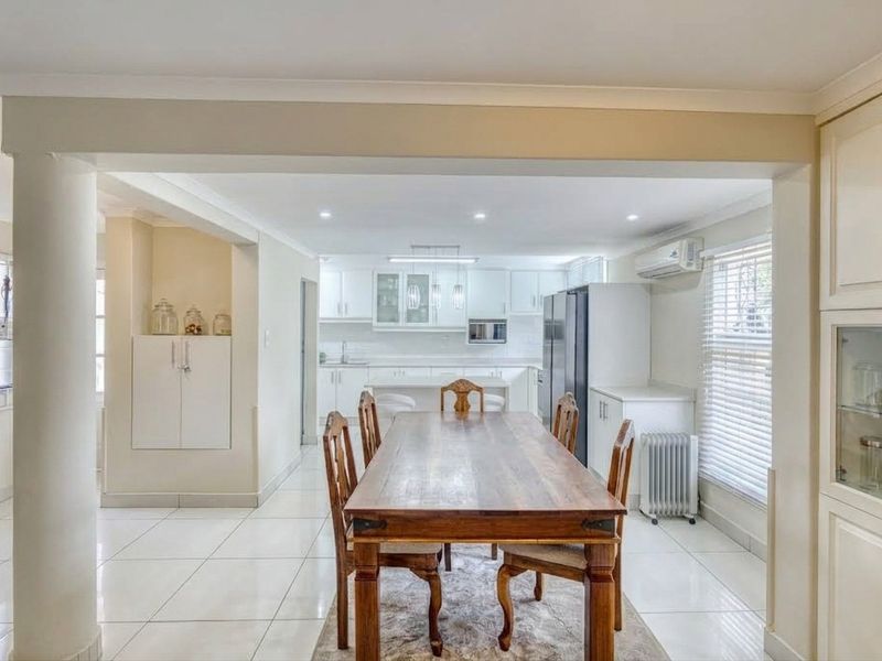 An open-plan kitchen and dining area featuring white cabinetry, tiled flooring, recessed lighting, and a structural column, creating a bright and functional living space.