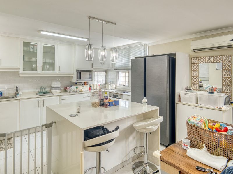 Modern kitchen featuring white cabinetry, stone countertops, a central island, subway tile backsplash, and integrated lighting, offering a clean and functional cooking space.