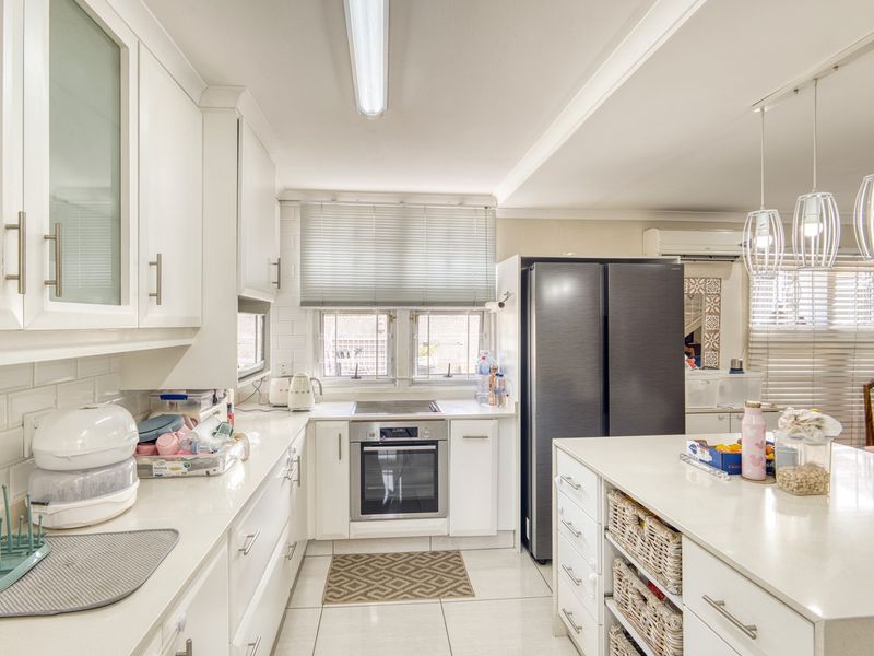 Modern kitchen featuring white cabinetry, quartz countertops, subway tile backsplash, a central island, and integrated appliances, offering a clean and functional cooking space.