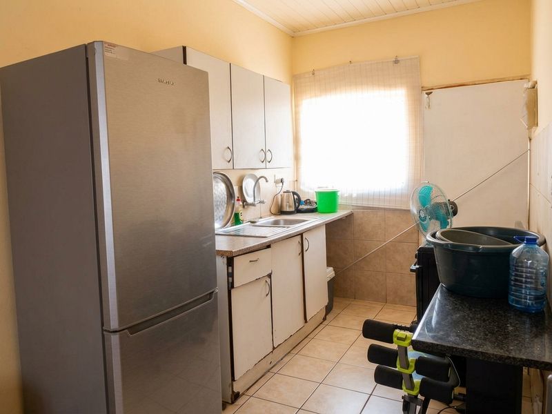 A compact kitchen featuring tiled flooring, a stainless steel sink, and built-in cabinetry with a tiled backsplash.