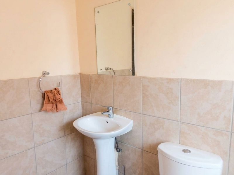 A functional bathroom featuring a pedestal basin with a chrome mixer tap, a wall-mounted mirror, and neutral ceramic wall tiling.