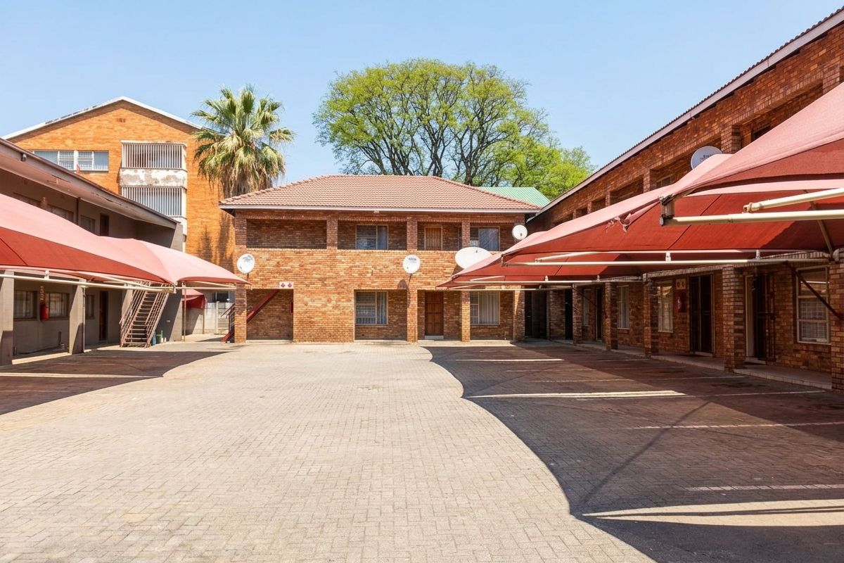 A view of the apartment complex courtyard featuring brick buildings, paved parking areas, and installed shade sail carports.