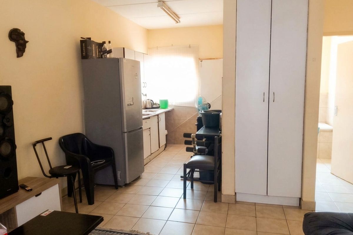 A functional kitchen area featuring tiled flooring, built-in cabinetry, and a tall storage cupboard, providing essential utility space within the apartment.