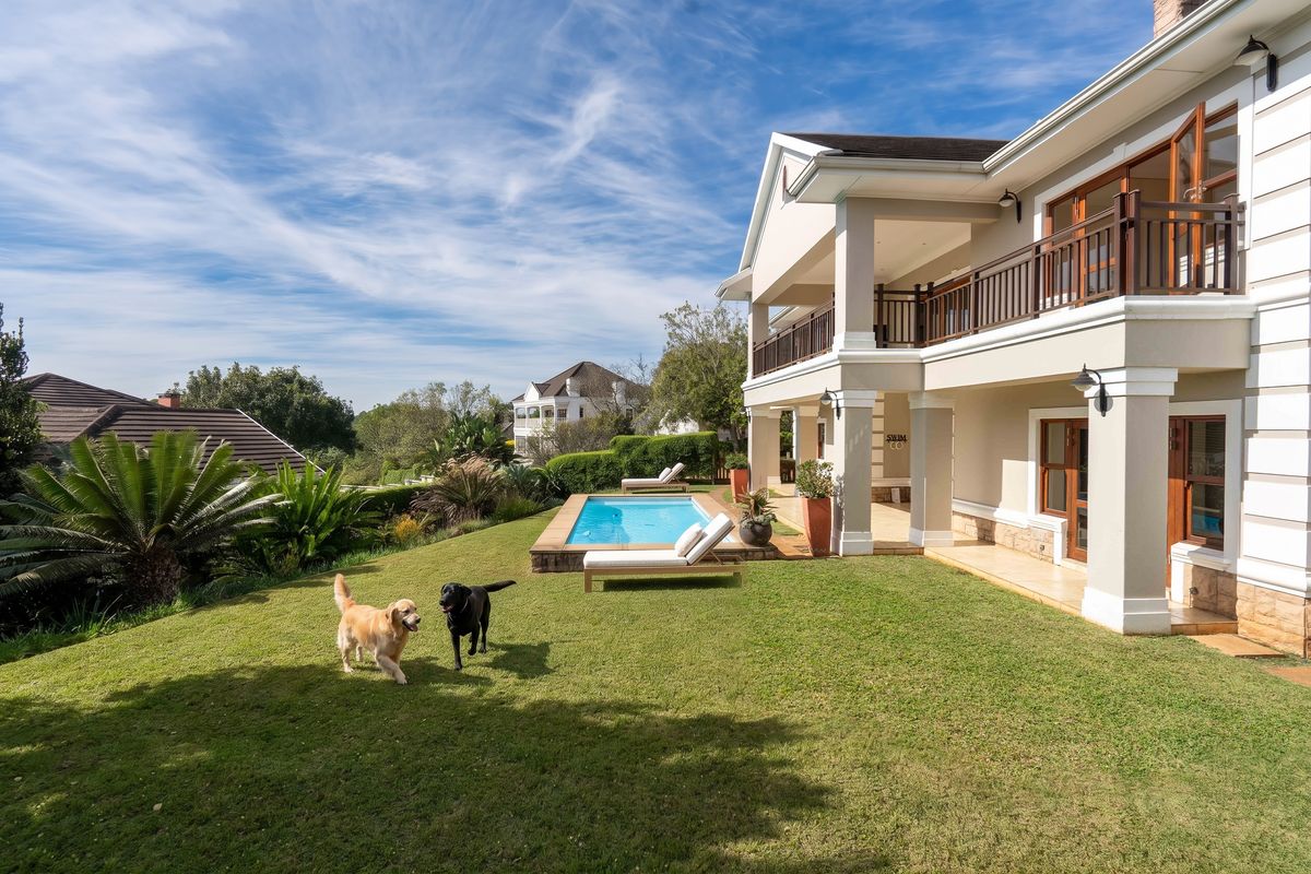 Spacious rear exterior featuring a well-maintained lawn, a swimming pool, and a double-story house with a covered patio and balcony.