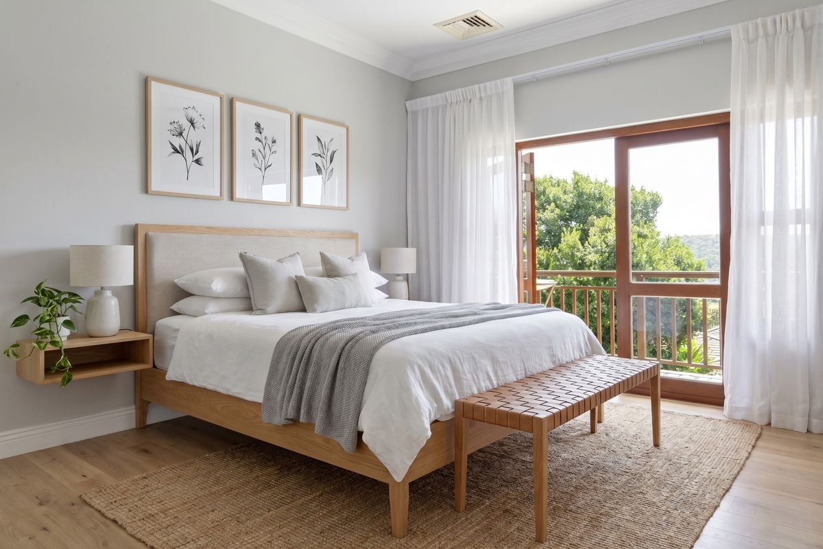 A bright and well-maintained bedroom featuring timber flooring, elegant ceiling cornicing, and direct access to a private balcony through timber-framed sliding doors.
