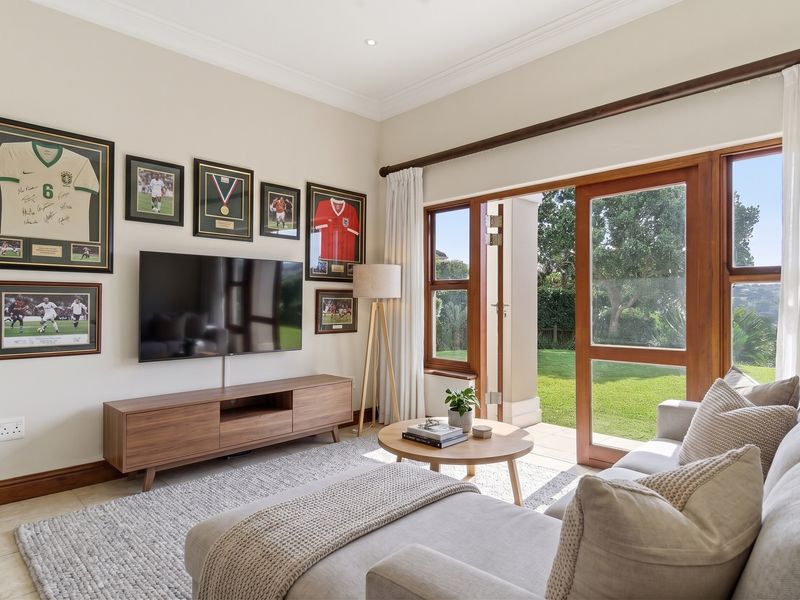 Bright living room featuring timber-framed sliding doors that open onto a garden patio, complemented by tiled flooring and coved ceiling details.
