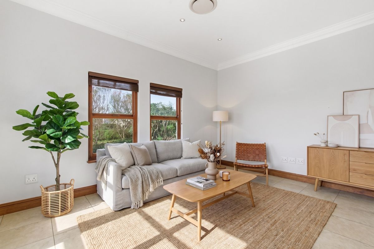 A bright and well-maintained living room featuring tiled flooring, timber-framed windows, and recessed downlighting, creating a comfortable and inviting atmosphere.