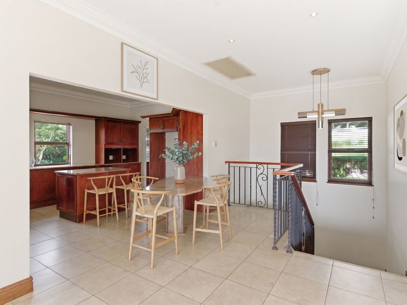 Open plan kitchen and dining area featuring warm wood cabinetry, stone countertops, tiled flooring, and a staircase with a decorative wrought iron balustrade.