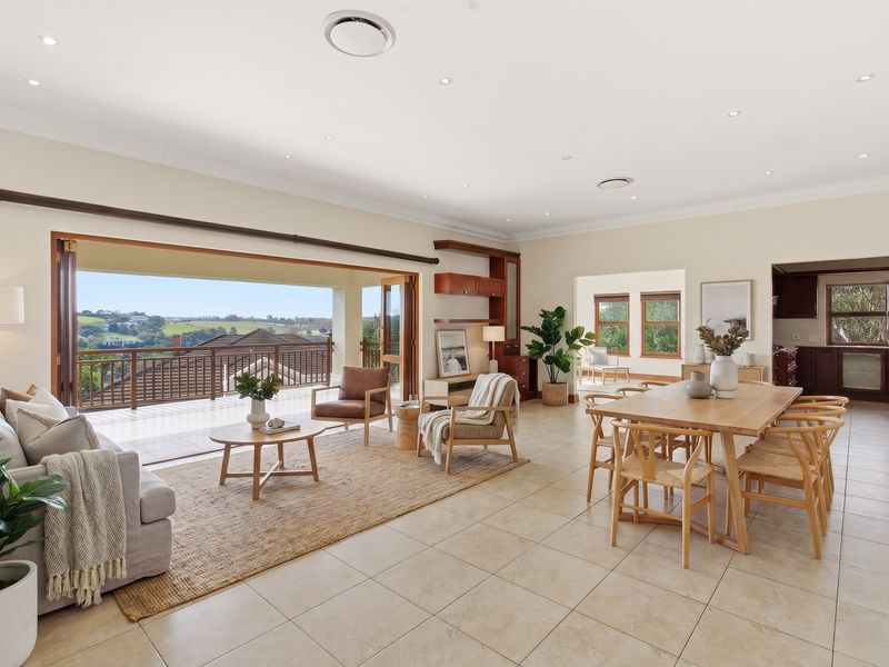 Spacious open-plan living and dining area featuring tiled floors, recessed lighting, and large bi-fold doors opening onto a balcony with scenic views.