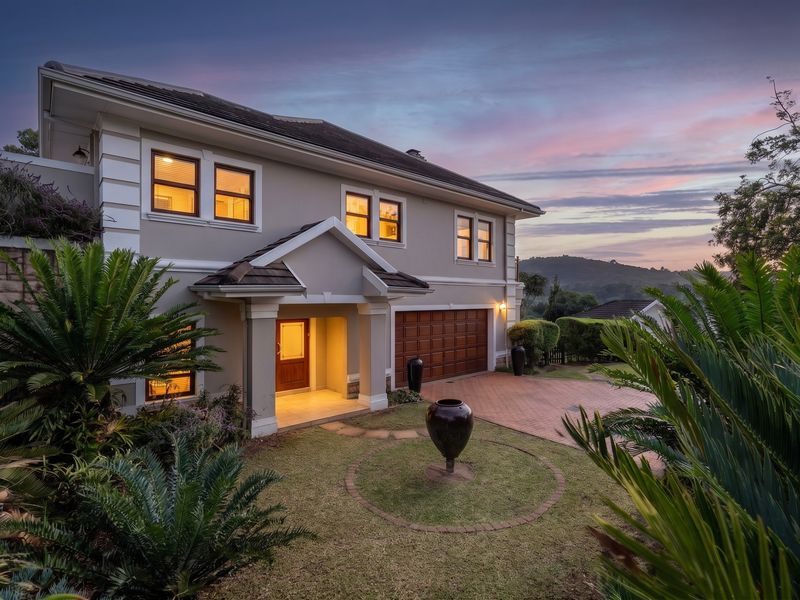 A well-maintained double-story house featuring a paved driveway, double garage, and an inviting covered entrance, set within a landscaped garden at dusk.