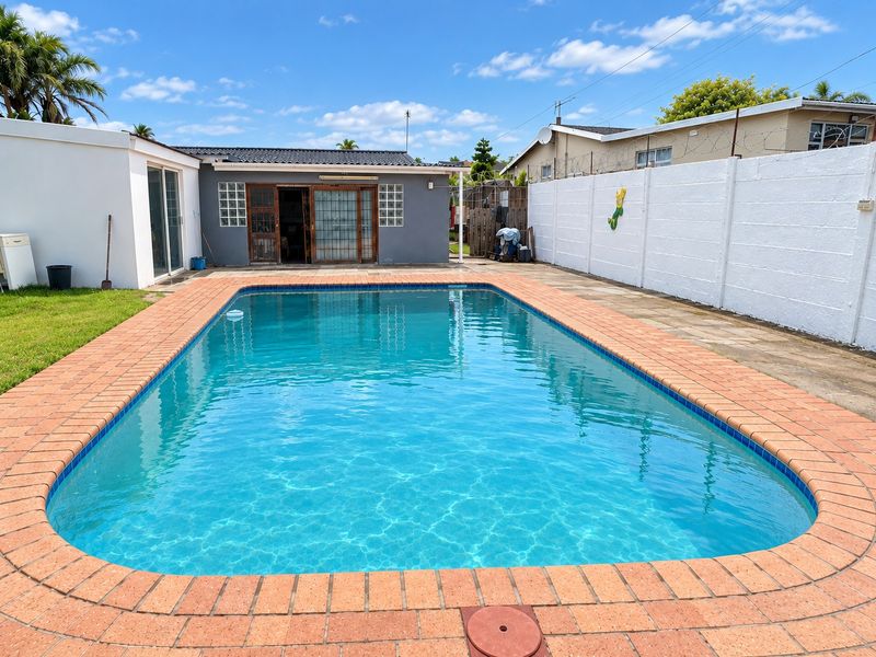 Outdoor pool area featuring a rectangular swimming pool with brick coping, surrounded by a paved patio and enclosed by a high boundary wall.