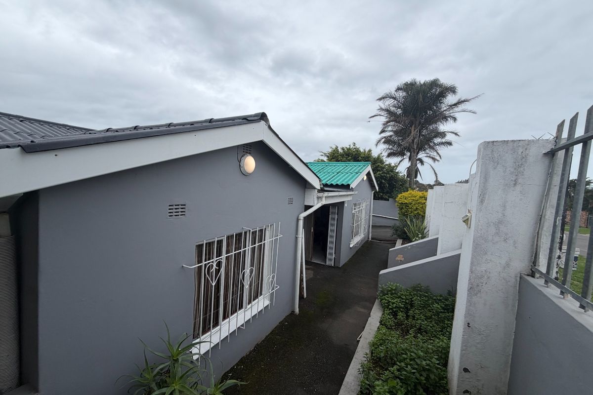 Rear exterior view of the property featuring a paved walkway, security bars on windows, and a boundary wall.
