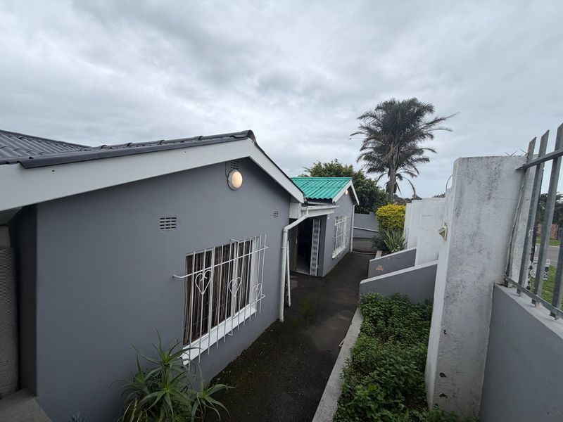 Rear exterior view of the property featuring a paved walkway, security bars on windows, and a boundary wall.