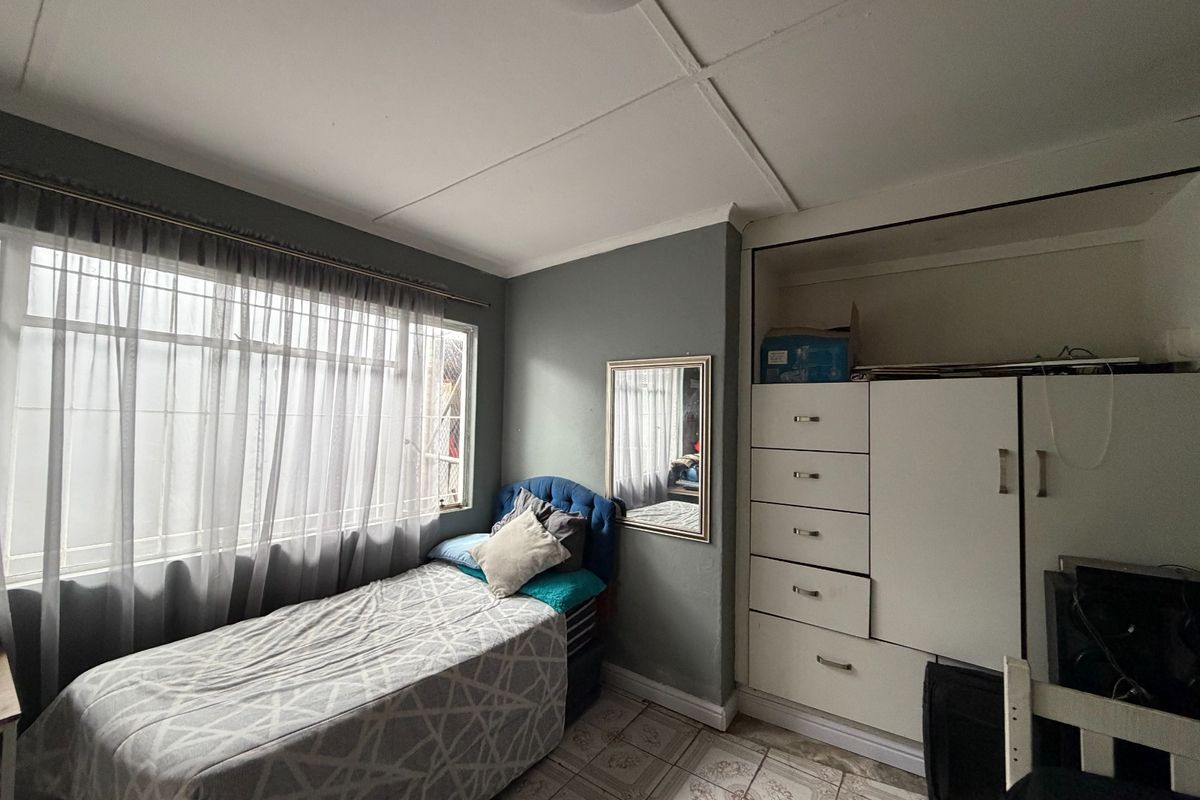 A bedroom featuring tiled flooring, a built-in wardrobe, and a window with sheer curtains. The ceiling shows visible signs of wear.