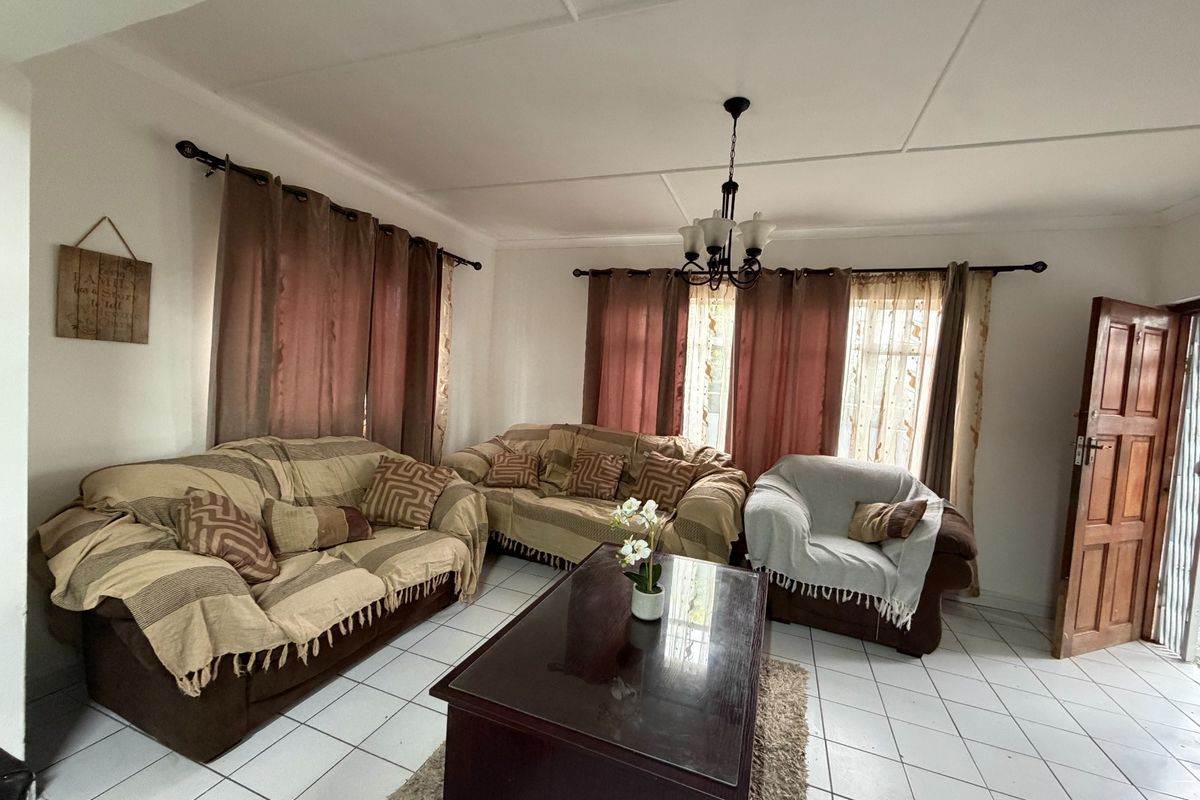 A living room featuring tiled flooring, a central chandelier, and natural light through windows with curtain rods.