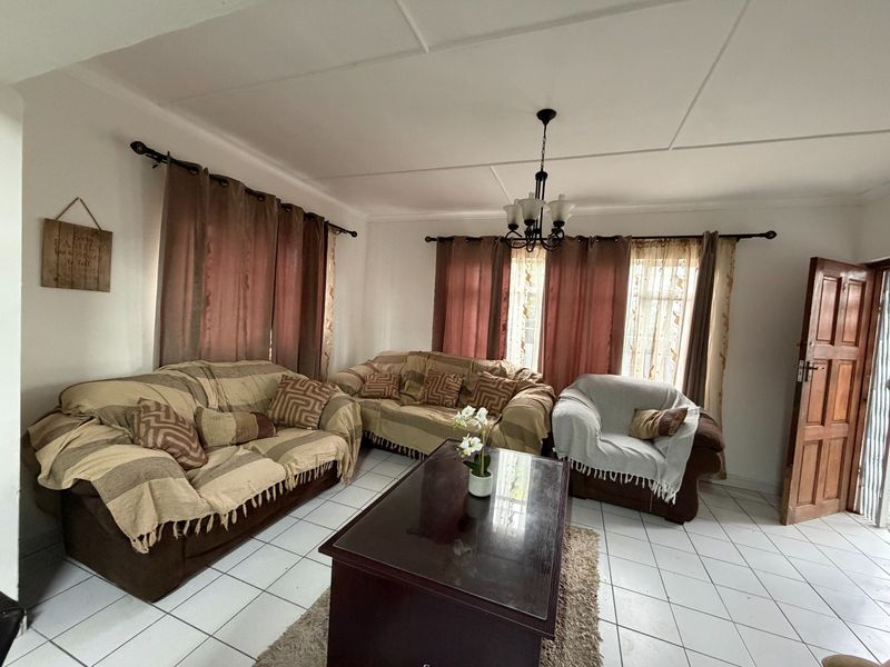 A living room featuring tiled flooring, a central chandelier, and natural light through windows with curtain rods.
