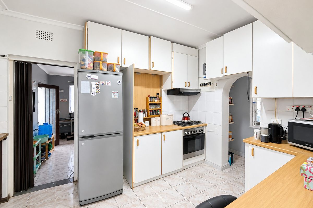 Functional kitchen featuring white cabinetry, laminate countertops, gas hob, built-in oven, and tiled flooring, with an adjacent archway leading to a secondary space.