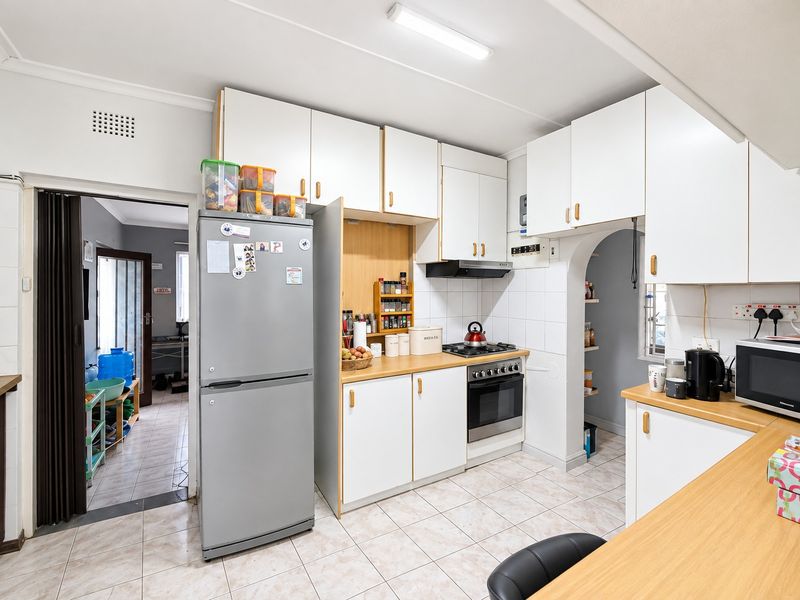 Functional kitchen featuring white cabinetry, laminate countertops, gas hob, built-in oven, and tiled flooring, with an adjacent archway leading to a secondary space.