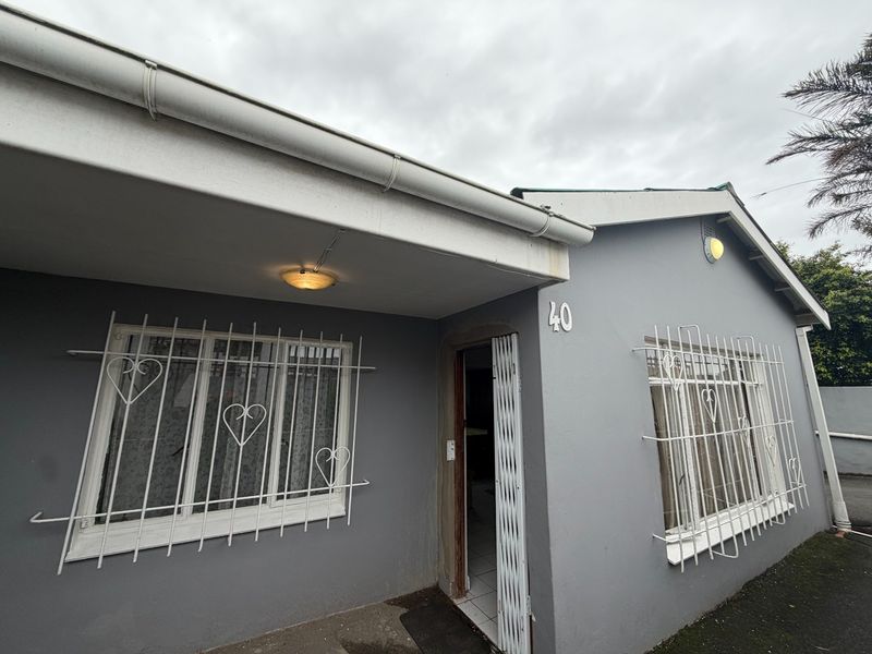 Front facade of a residential property featuring grey painted walls, security bars on windows, and a covered entrance area.