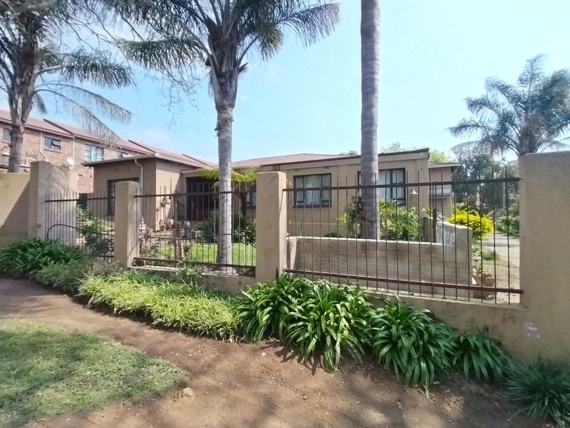 Front view of a single-story house featuring plastered walls, a tiled roof, and metal perimeter fencing with concrete pillars.