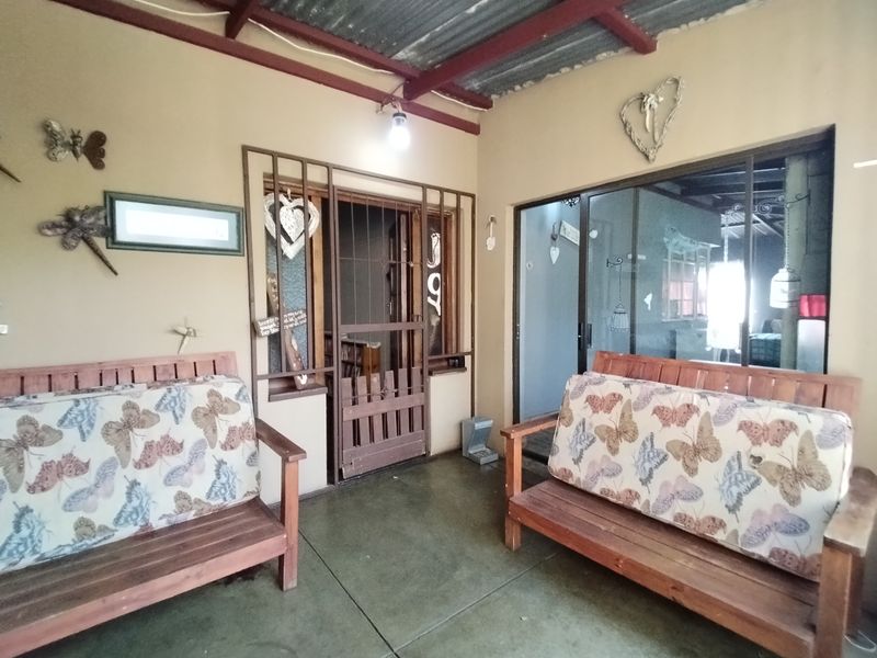 A covered patio area featuring exposed timber rafters, concrete flooring, and secure access points through a security gate and sliding glass doors.