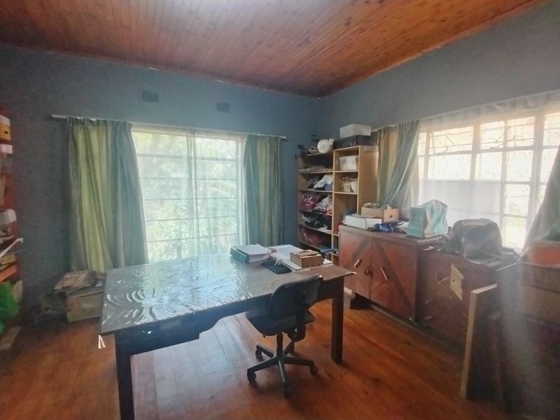 A home office space featuring timber flooring, a wood-paneled ceiling, and natural light provided by a sliding glass door and steel-framed windows.