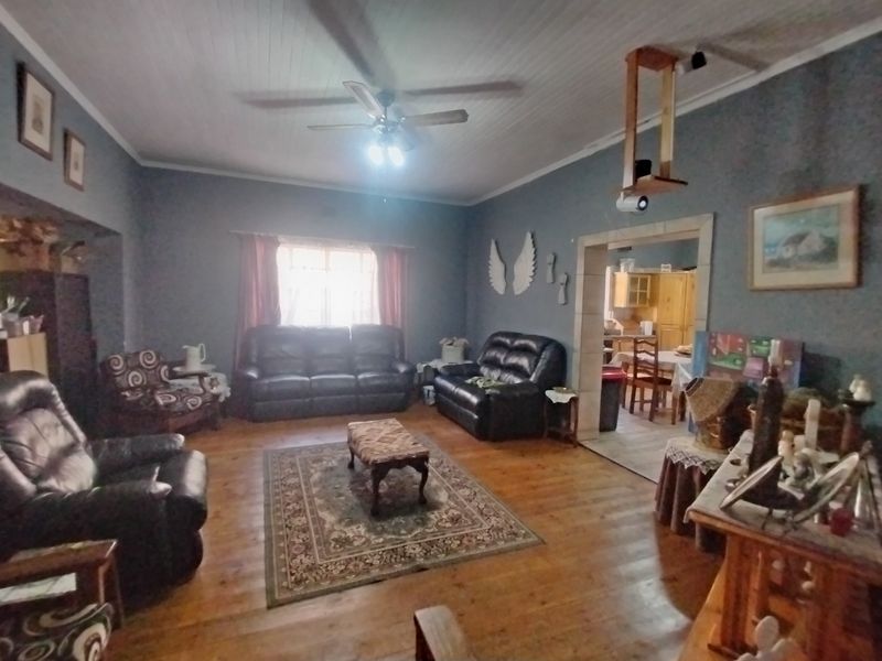 Spacious living room featuring warm timber flooring, a classic tongue and groove ceiling, and an open archway leading to the adjacent dining area.