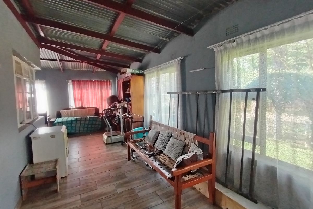 A living area featuring exposed timber rafters, corrugated metal ceiling, tiled flooring, and large windows with security bars.