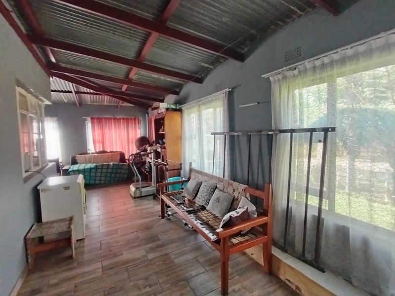 A living area featuring exposed timber rafters, corrugated metal ceiling, tiled flooring, and large windows with security bars.