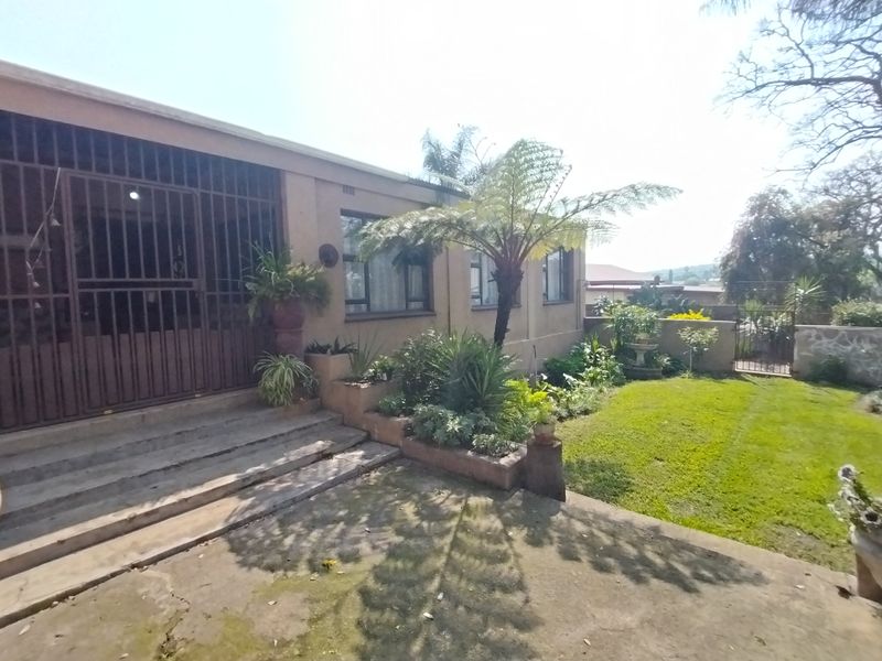 A rear exterior view featuring a concrete patio, established garden with lawn, and a secure entrance with metal security gate.