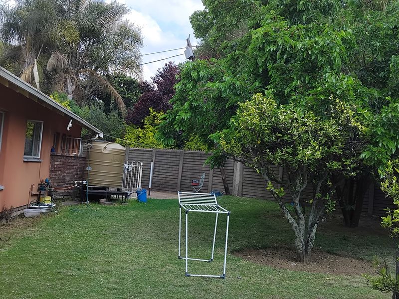 Rear garden area featuring a lawn, mature trees, boundary wall, and an external water storage tank.