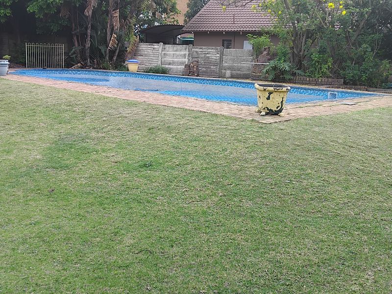 A backyard area featuring a swimming pool with brick coping, set within a grassed garden and enclosed by precast concrete boundary walls.