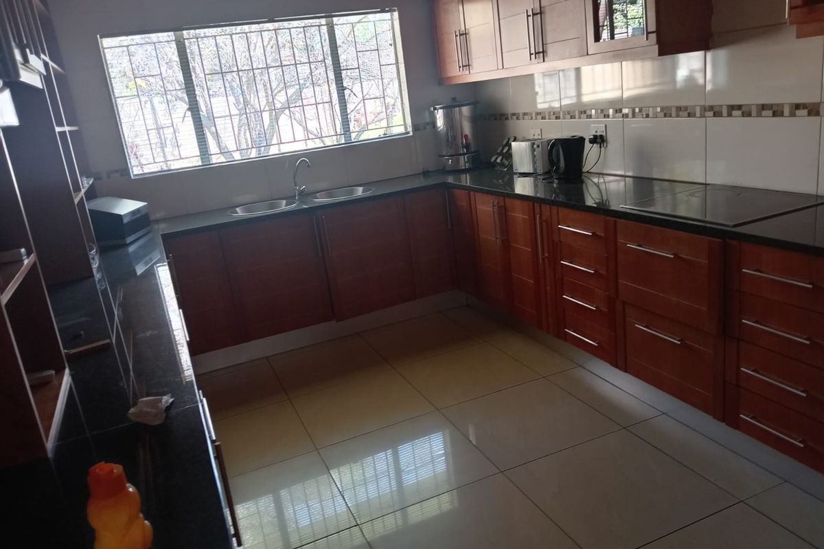 A functional kitchen featuring warm-toned wooden cabinetry, granite countertops, a double basin sink, and tiled flooring with a large window for natural light.
