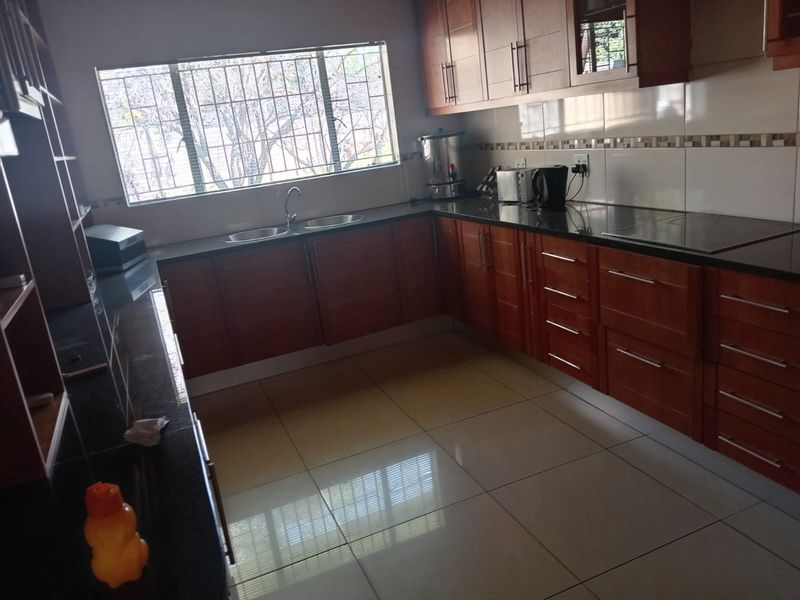 A functional kitchen featuring warm-toned wooden cabinetry, granite countertops, a double basin sink, and tiled flooring with a large window for natural light.