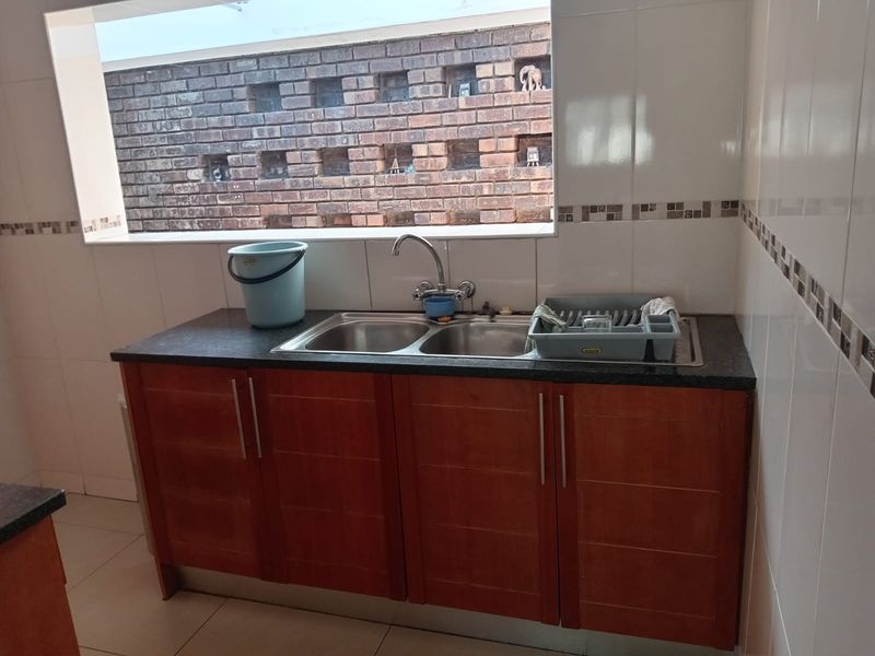 A functional scullery area featuring a double bowl stainless steel sink, granite countertops, and wood-finish cabinetry with tiled splashbacks.