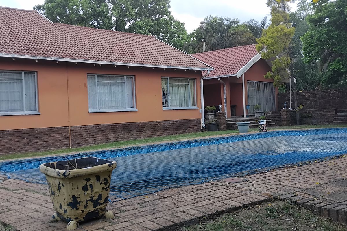 Rear view of the house featuring a swimming pool with a safety net, brick paving, and a tiled roof structure.