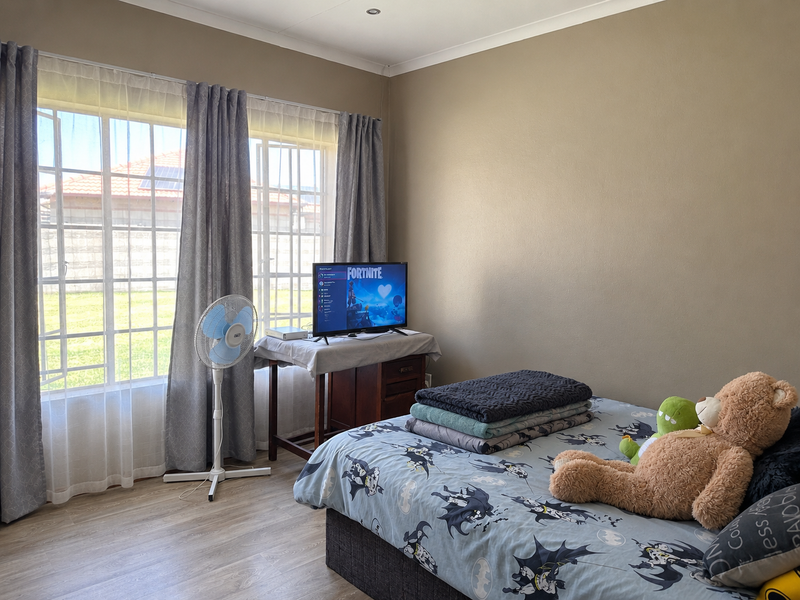 A bedroom featuring laminate flooring, recessed ceiling lights, and a large window with grid detailing, providing natural light to the space.