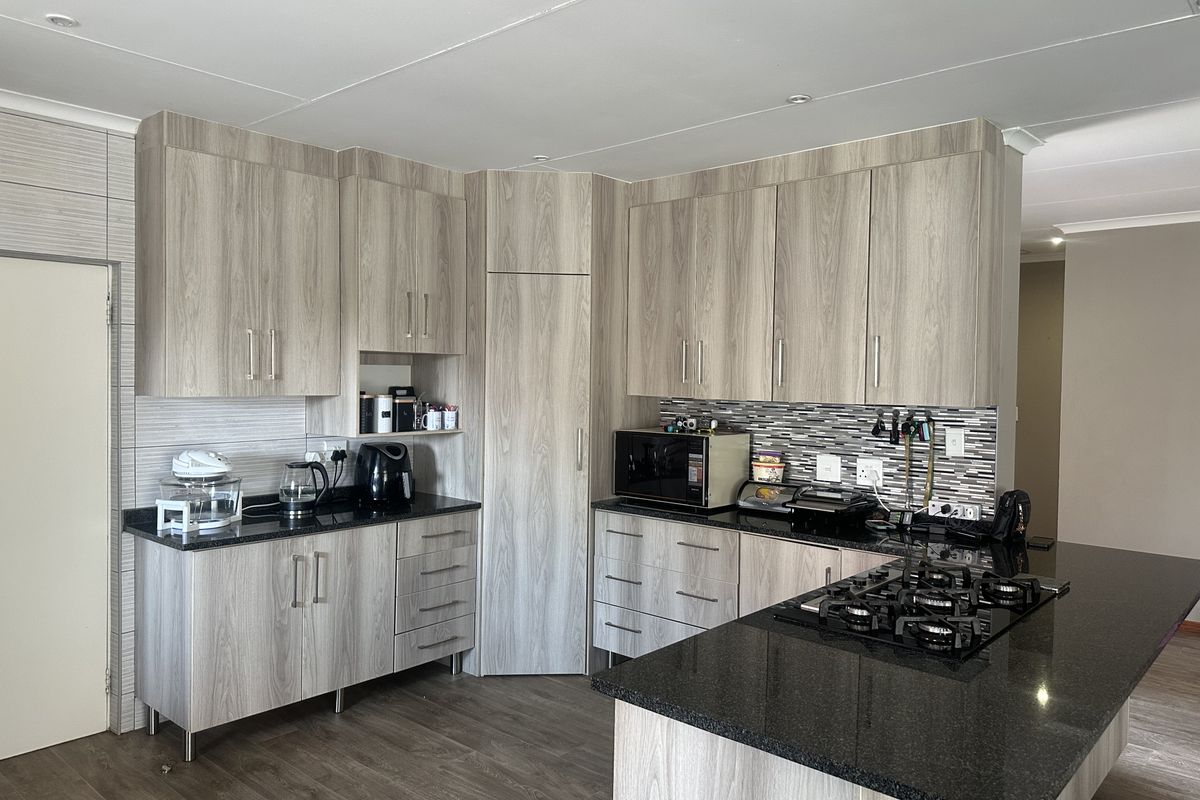 Modern kitchen featuring light wood-grain cabinetry, dark granite countertops, a gas hob, and a stylish mosaic tile backsplash.