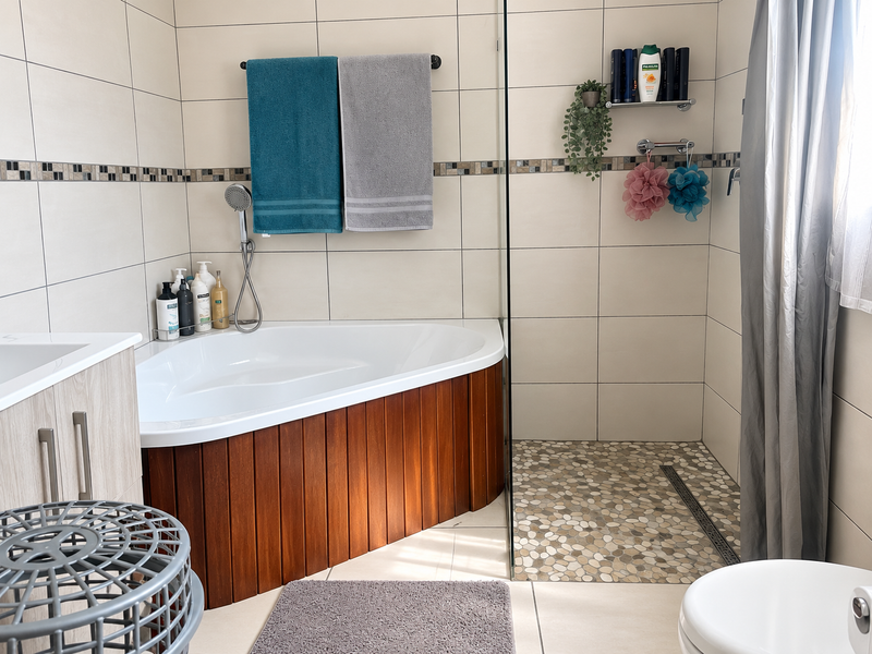 Modern bathroom featuring a corner bathtub with wood-panel finish, a walk-in shower with pebble flooring, and neutral wall tiling.