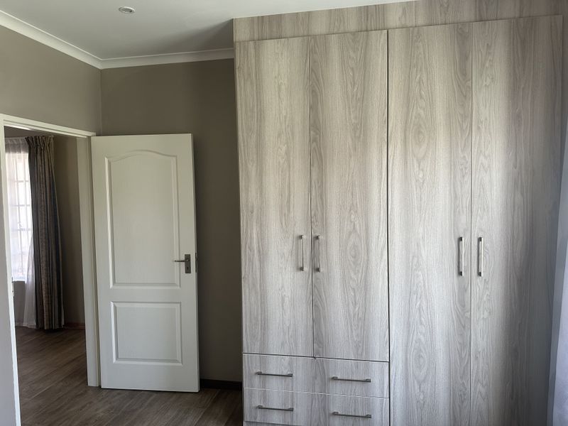 A clean bedroom featuring modern wood-grain built-in cupboards, laminate flooring, and neutral wall tones, offering a bright and functional living space.