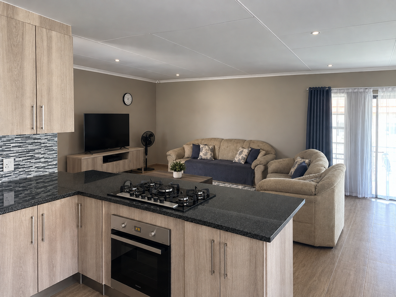 Modern open-plan living area featuring a well-appointed kitchen with granite countertops, gas hob, and built-in oven, flowing seamlessly into a comfortable lounge space.