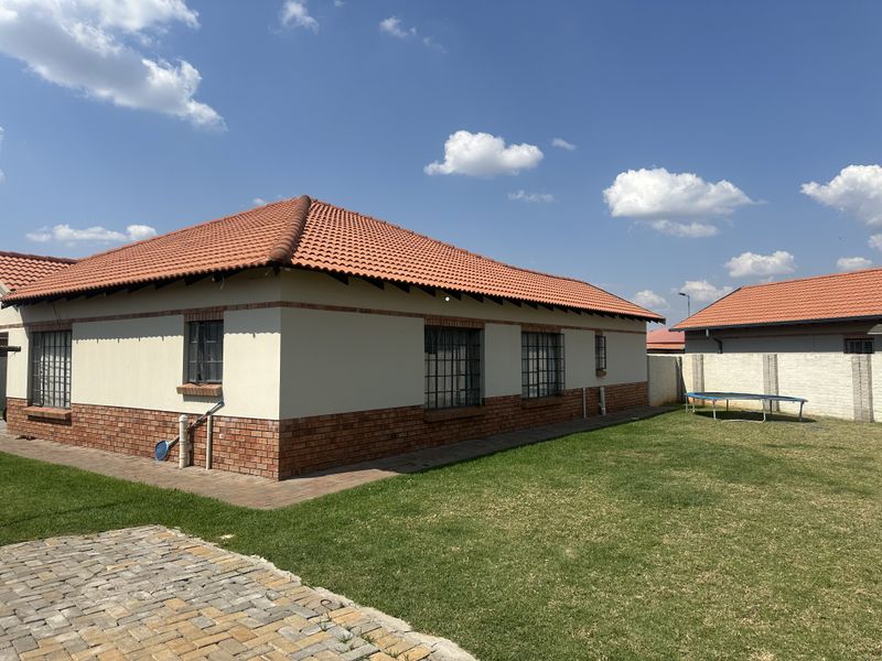 Rear view of the house featuring a well-maintained lawn, paved walkway, and a tiled roof with brick and plaster exterior walls.