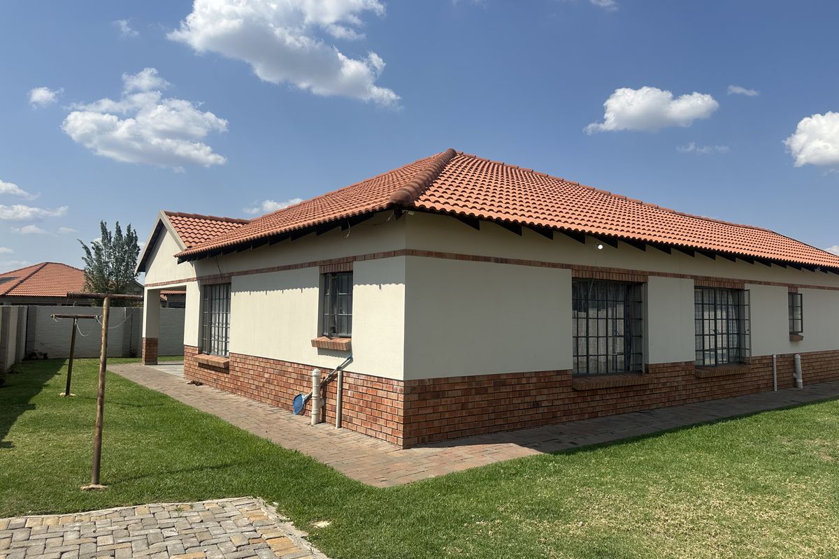 Rear view of a single-story house featuring a terracotta tiled roof, brick base, and security-barred windows, set within a well-maintained garden.