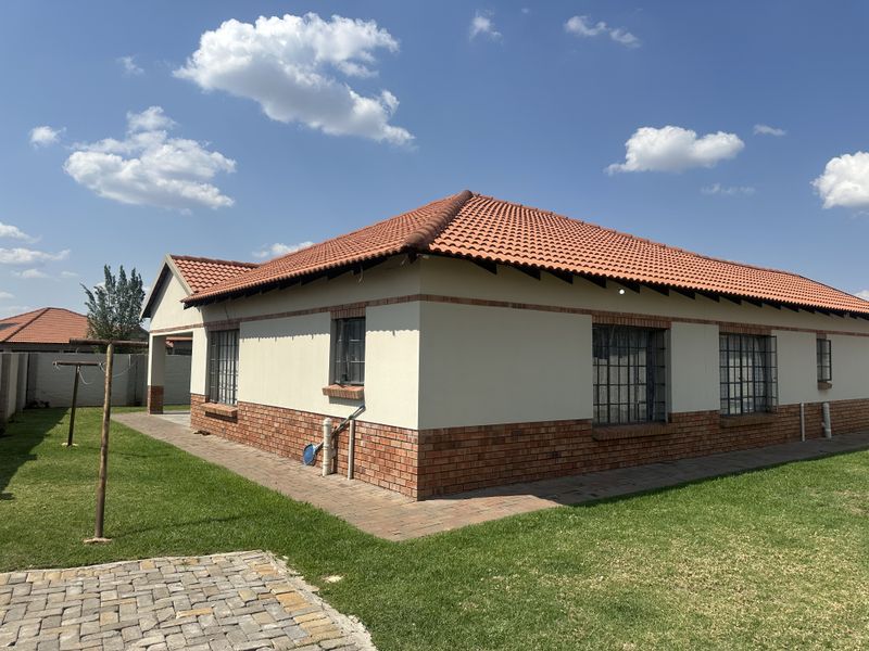 Rear view of a single-story house featuring a terracotta tiled roof, brick base, and security-barred windows, set within a well-maintained garden.