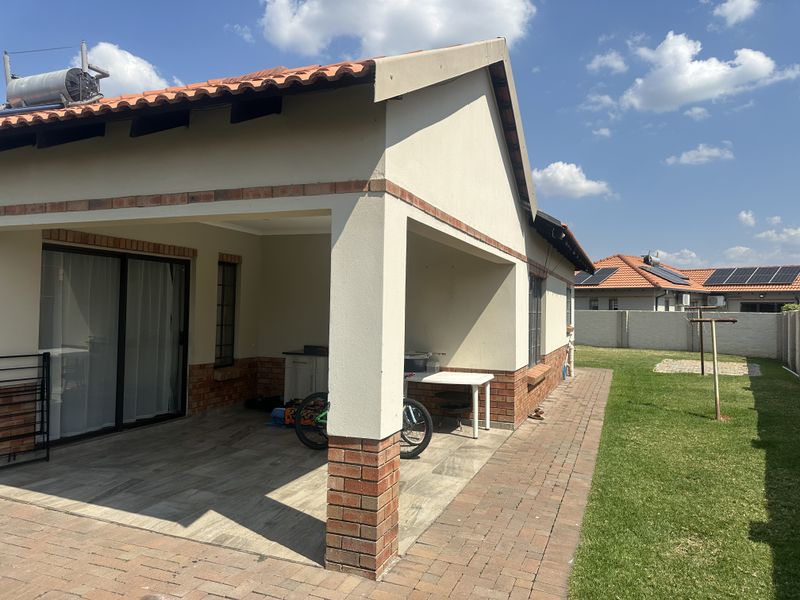 A covered patio area featuring brick accents and tiled flooring, leading out to a well-maintained garden with paved pathways.