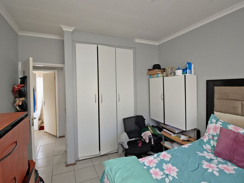 A bedroom featuring built-in cupboards, tiled flooring, and coved ceiling details, providing a functional space with direct access to an adjacent room.