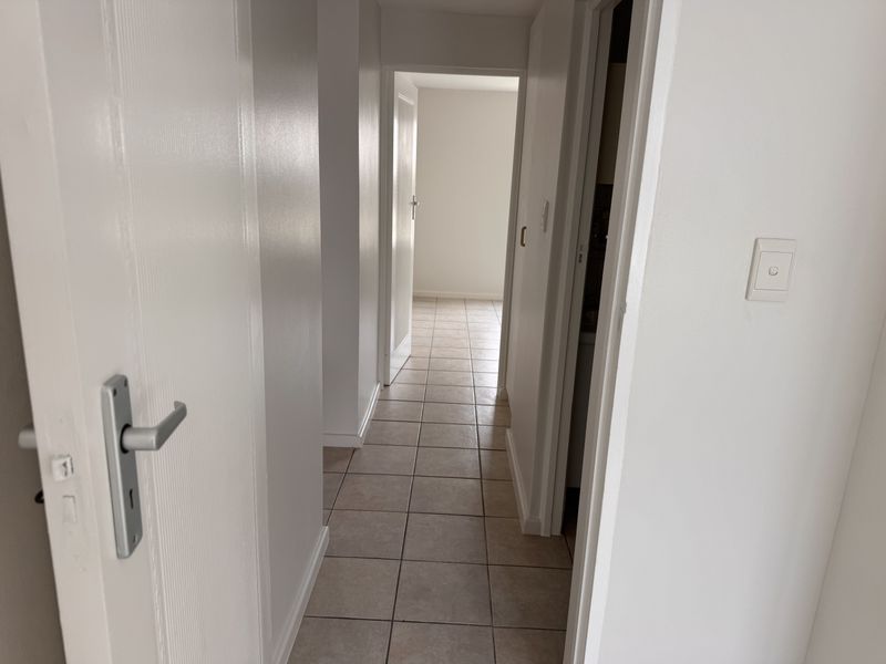 A clean, neutral hallway featuring tiled flooring and multiple internal doorways, providing access to various rooms within the apartment.