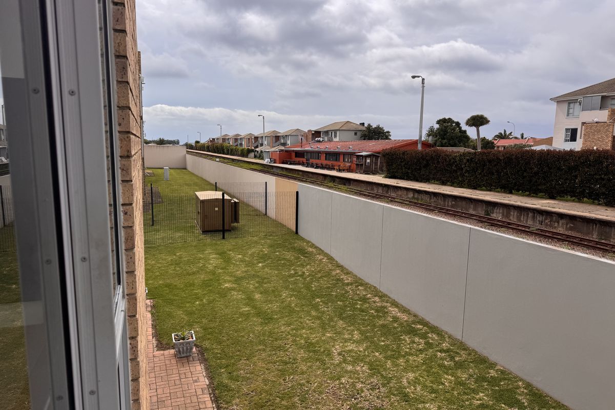 View of the rear garden area featuring a lawn, paved path, and perimeter wall, adjacent to a railway line.