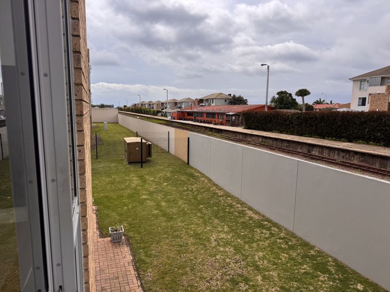 View of the rear garden area featuring a lawn, paved path, and perimeter wall, adjacent to a railway line.